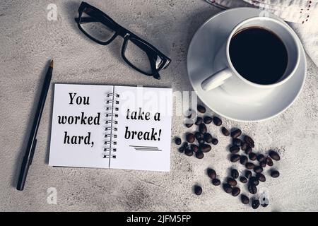 Una citazione ispiratrice sul blocco note con caffè e caffè sulla scrivania bianca: Hai lavorato sodo, fai una pausa. Foto Stock