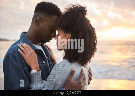 Affettuosa coppia multietnica in piedi con gli occhi chiusi su una spiaggia al crepuscolo Foto Stock