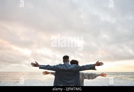 Giovane coppia multietnica in piedi con le braccia sollevate su una spiaggia Foto Stock