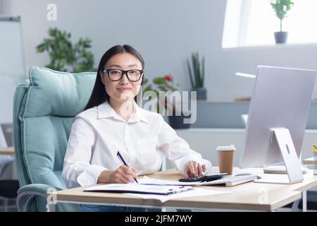 Ritratto di giovane bella e di successo donna di affari asiatica, dipendente femminile sorridendo e guardando la macchina fotografica, contabile finanziere lavoro di carta. Foto Stock