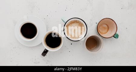 Vista dall'alto su piatto con molte diverse tazze da caffè piene e vuote su sfondo grigio bianco di cemento. Varietà di tea tazza disposizione collezione. Chicchi di caffè secchi. Espresso, latte, americano Foto Stock