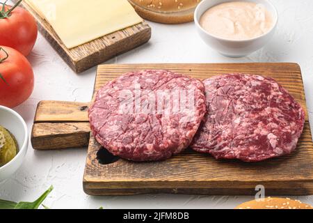 Hamburger crudi di carne di manzo macinati, su sfondo di pietra bianca Foto Stock