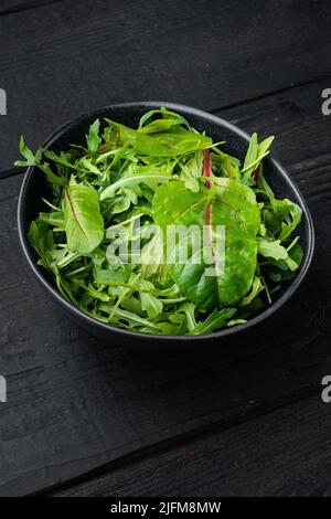 Insalata verde alle erbe con rucola e mangold, bietola svizzera, su fondo nero di legno Foto Stock
