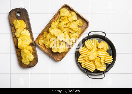 Patatine fritte aromatizzate all'aceto di sale sullo sfondo di un tavolo con piastrelle quadrate in ceramica bianca, vista dall'alto su una superficie piana Foto Stock