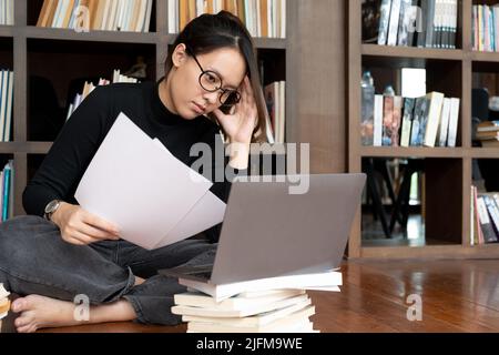 Studente che studia esame duro, dorme su libri letto in biblioteca. Donna esausta che ha un mal di testa. Foto Stock