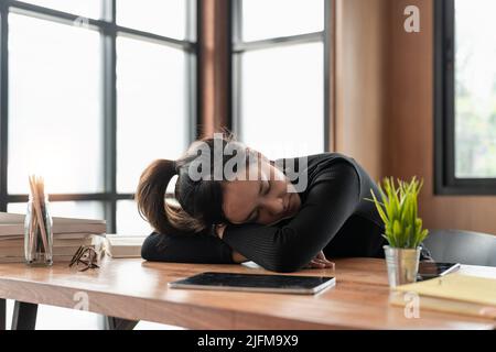 Esausta, stressata giovane donna asiatica d'affari che lavora, ha tollato gli occhiali strain, riposo nap, dormire sulla scrivania dopo il lavoro duro mentre si usa il computer portatile Foto Stock