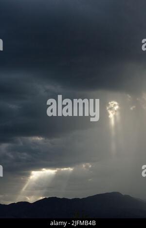 Nuvole di tempesta sulle montagne con travi di sole che pocchano attraverso. Foto Stock