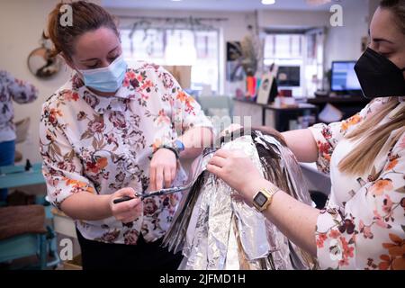 Un primo piano di due parrucchieri professionali che tingendo i capelli di una donna cliente in salone Foto Stock