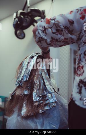 Un colpo verticale di un parrucchiere professionale che tinge i capelli di una donna cliente in salone Foto Stock