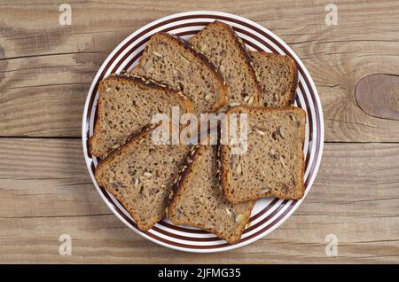Fette di pane di segale con semi diversi in un piatto su vecchio sfondo di legno, vista dall'alto Foto Stock