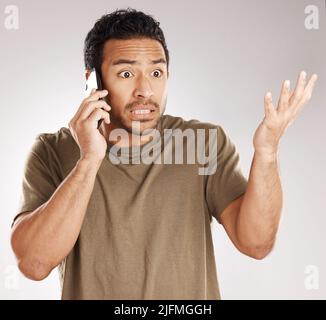 Bel giovane uomo misto da corsa che guarda irritato, aggravato o agitato mentre usando il suo telefono in studio isolato su uno sfondo grigio. Dispiaciuto Foto Stock