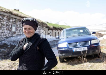 Donna anziana in piedi di fronte alle sue belle case tradizionali con tetto in erba unica nel villaggio di Tambovka al lago Paravani, Javakheti, Georgia Foto Stock