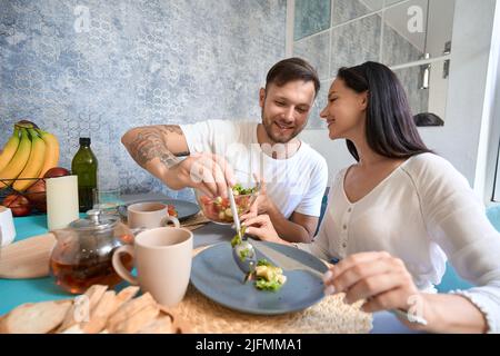 Uomo amorevole che si cura della moglie e che riempie il piatto di cibo Foto Stock