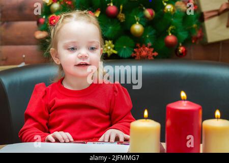 Una ragazza guarda le candele brucianti in una serata di Natale con interesse e curiosità. Foto Stock