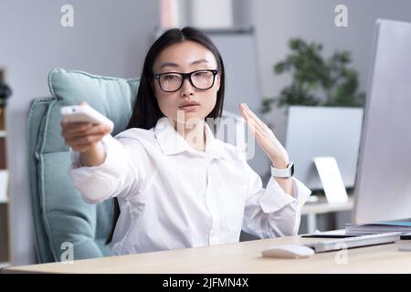 Il calore in ufficio, un responsabile di affari, una donna commuta il pannello di controllo di aria condizionata, raffredda la stanza, un impiegato lavora nell'ufficio. Foto Stock