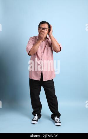 L'uomo asiatico adulto con camicia rosa in piedi su sfondo blu. Foto Stock
