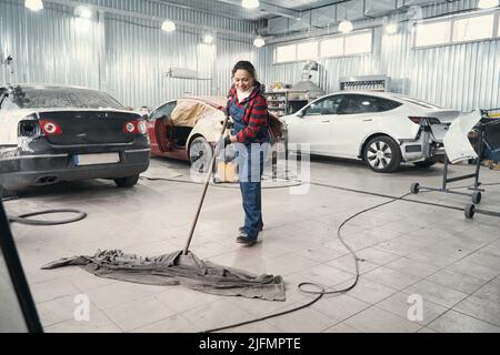 Felice donna pulizia pavimento in officina Foto Stock