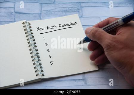 Testo delle risoluzioni dell'anno nuovo su un blocco note con una mano che tiene una penna. Concetto di risoluzione e spazio di copia per il nuovo anno Foto Stock