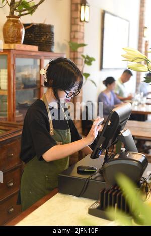 Giovane cameriera vietnamita che serve un cliente al check-out in caffetteria Foto Stock
