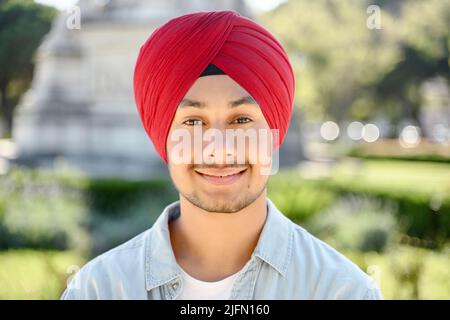 Giovane simpatico ragazzo sikh in tradizionale testa avvolge turban guardando la macchina fotografica e sorrisi, ritratto da vicino di sereno felice studente indiano maschio, imprenditore in piedi all'aperto Foto Stock