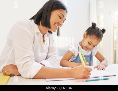 Madre mista di razza che aiuta sua figlia con i suoi compiti. Mamma insegnando a figlia di leggere e scrivere durante la classe homeschool. Bambina seduta a casa Foto Stock