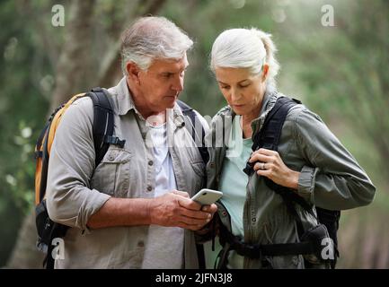 Una coppia matura usando un cellulare mentre fuori su un'escursione insieme. Marito e moglie caucasici senior che utilizzano un dispositivo wireless in una foresta Foto Stock