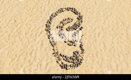 Pietre concettuali o concettuali sulla spiaggia sabbia forma simbolo fatta a mano, sfondo sabbioso dorato, segno di un orecchio. 3d metafora illustrativa per la perdita dell'udito Foto Stock