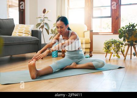 Promuovere una maggiore flessibilità e mobilità. Scatto di una giovane donna sportiva che allunga le gambe mentre si esercita a casa. Foto Stock