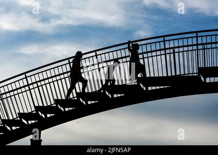 Tre bambini come silhouette che saliscono sui gradini di un grande ponte di metallo contro un cielo blu con nuvole, sfida futura per la prossima generazione c Foto Stock