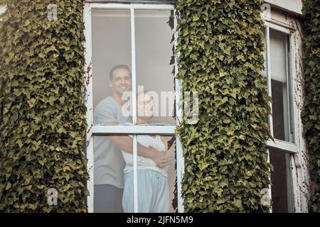 Felice giovane coppia di gara mista in piedi nella loro finestra. Coppia di amore che si lega e passare il tempo insieme a casa. Gli amanti in piedi da una finestra con Foto Stock