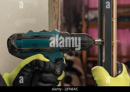 Foratura di un foro nella porta con un cacciavite verde, primo piano del processo di foratura, installazione di porte interne. Foto Stock