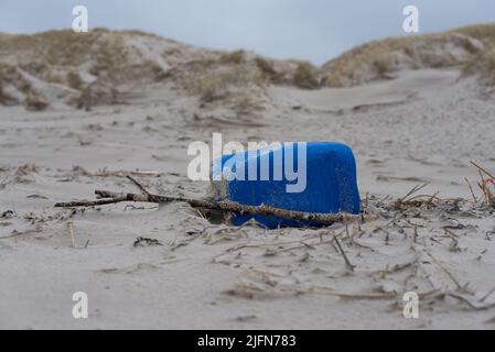 primo piano di un barattolo di plastica blu lavato / jerrycan sulla spiaggia di fronte alle dune di sabbia Foto Stock