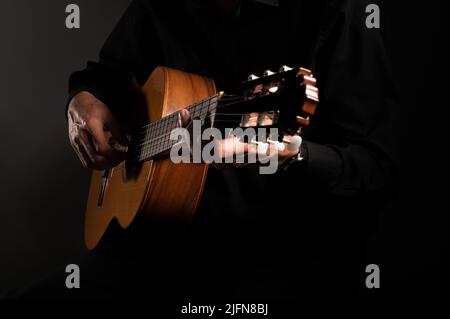 La chitarra classica spagnola e il chitarrista si avvicinano da vicino su uno sfondo nero con spazio copia Foto Stock