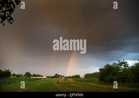 Grandi balle rotonde di paglia nel prato con incredibile arcobaleno - campo raccolto con balle di paglia in estate Foto Stock