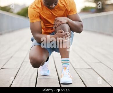 Un pareggiatore con dolore al ginocchio. Un uomo afroamericano che afferra il ginocchio in dolore dall'esercitarsi. Un pareggiatore con dolore al ginocchio. Un uomo afroamericano che afferra Foto Stock