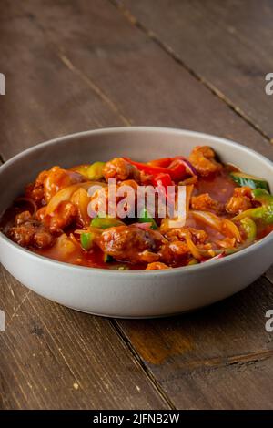 Un colpo verticale di pollo kung pao in una ciotola bianca posta su un tavolo di legno Foto Stock