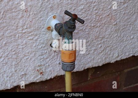 Vecchio rubinetto esterno in metallo arrugginito collegato a un tubo da giardino giallo Foto Stock