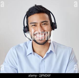 Ritratto di un giovane agente di call center misto che lavora nel suo ufficio. Operatore al suo lavoro di ricezione. Uomo ispanico che indossa una cuffia wireless sorridente Foto Stock