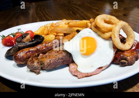 Una tradizionale grigliata mista inglese. Un classico pasto da pub britannico. Il piatto contiene quattro diverse carni alla griglia, un uovo fritto, patatine fritte, anelli di cipolla fritti Foto Stock