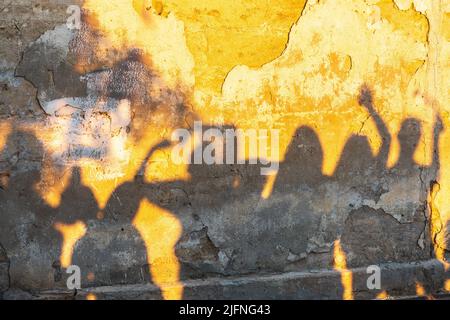 Ombre di danzanti su una vecchia parete al tramonto. Gruppo di ombre umane sullo sfondo del muro di pietra. Foto Stock