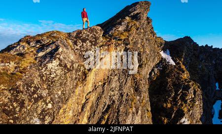 Escursionista che si affaccia su incredibili montagne illuminate dal sole di mezzanotte a Reinebringen, Lofoten, Norvegia Foto Stock