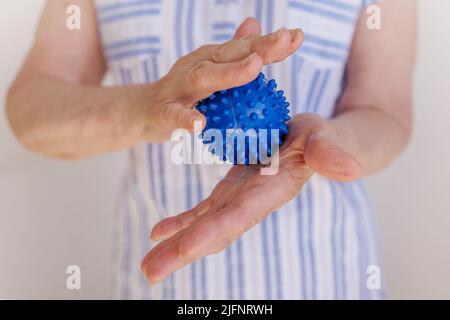 donna anziana spreme una pallina pungente nelle mani, auto-massaggio con parkinson Foto Stock
