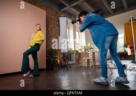 Giovane fotografo che prende le foto di modello, backstage di fotografare in studio. Foto Stock