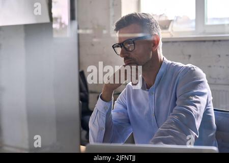 Uomo d'affari attento che lavora usando il calcolatore nell'ufficio moderno al tavolo. Foto Stock