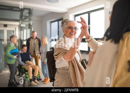 Buone donne studenti anziani che incontrano alto fiving in corridoio all'università. Foto Stock