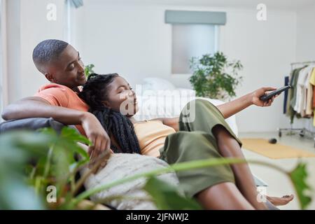 Giovane coppia afroamericana che cambia canale in remoto e guarda la televisione insieme sul divano a casa. Ragazza rilassante sul giro dei fidanzati Foto Stock