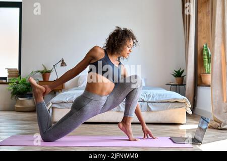 Donna africana che fa l'esercizio di yoga a casa guardando la classe virtuale sul laptop. Foto Stock