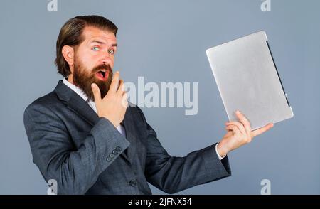 Uomo sorpreso con il computer portatile. Uomo d'affari in abito formale con notebook. Tecnologia, internet. Foto Stock