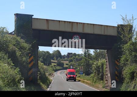 Un furgone rosso si avvicina sotto un ponte ferroviario in metallo. C'è una limitazione di altezza di 4,2 metri sul ponte Foto Stock