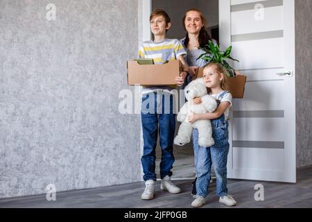 La famiglia si sposta in un nuovo appartamento, una bambina corre nella porta, tenendo scatole di cartone sullo sfondo. Madre con suo figlio e figlia Foto Stock